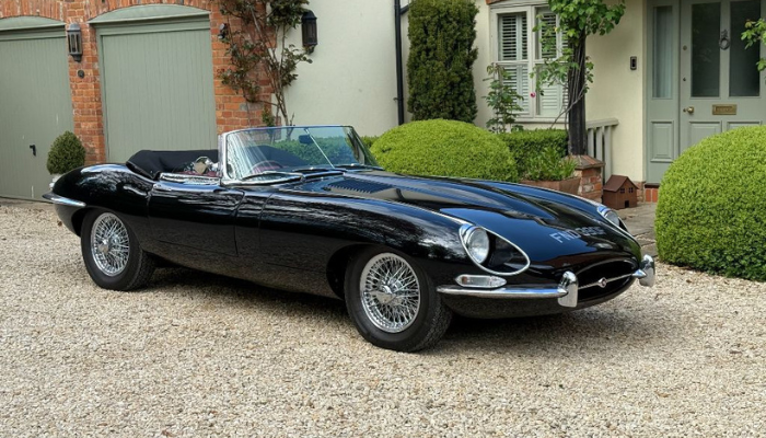 Black convertible Jaguar e-type with wire rims and chrome brightwork. With roof down. 